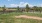 a fenced in field with a dirt path and trees and a house in the background